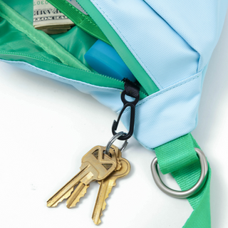 Close-up of keys clipped to a carabiner on the green D-ring of a light blue fanny pack